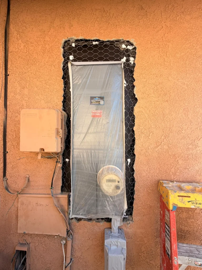 Exterior electrical panel protected with plastic while the surrounding stucco is being repaired.